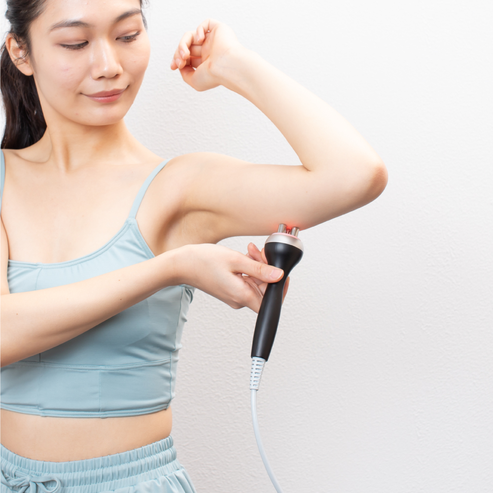 二の腕にマッサージ機を当てている女性